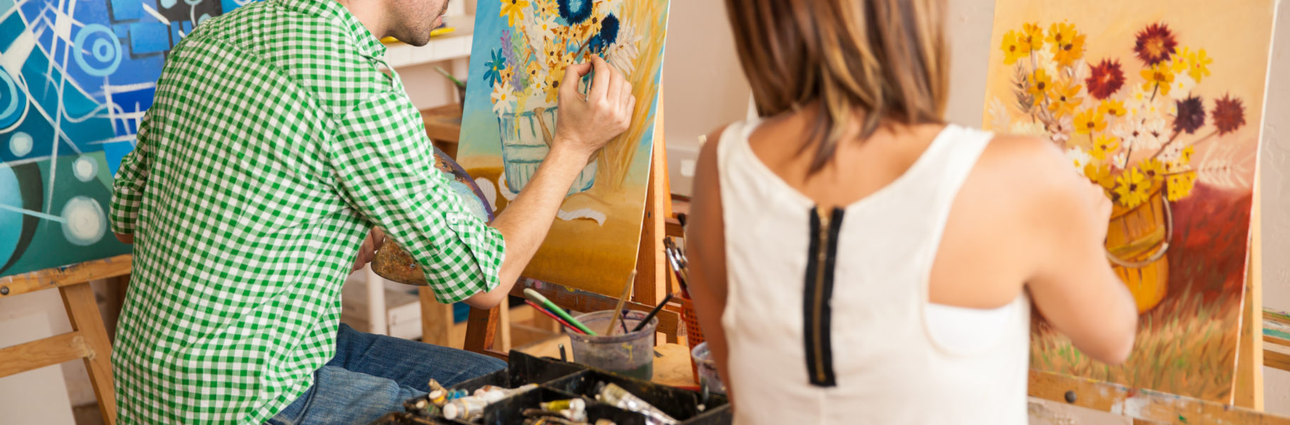 Rear view of a couple of young adults working on their own paintings while studying at an art school